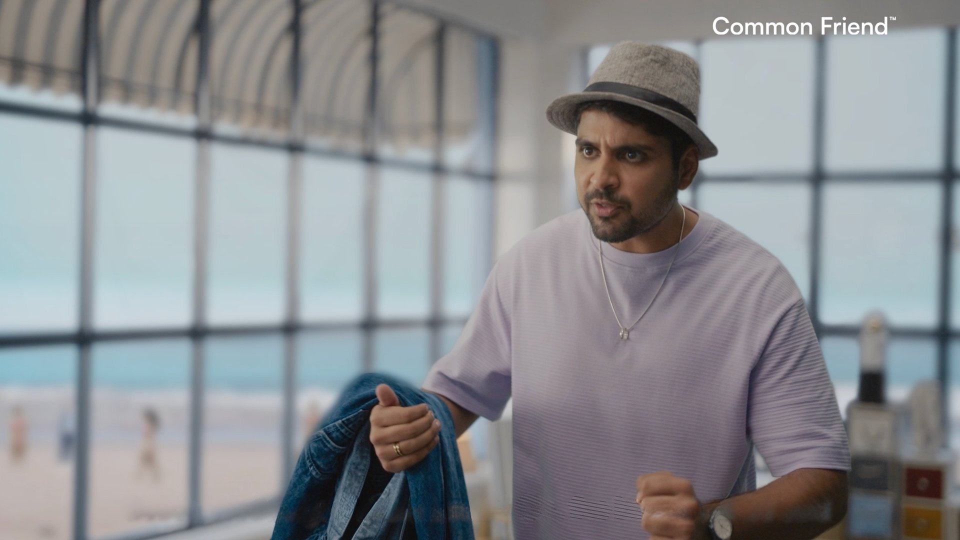 Male character standing inside beach farmhouse commercial set with diffused daylight and ocean background.