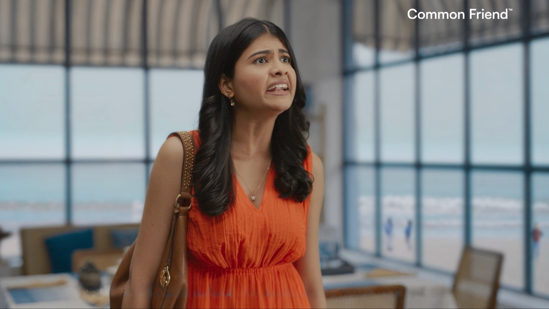 Female character in orange dress inside beach farmhouse set during emotional confrontation scene.