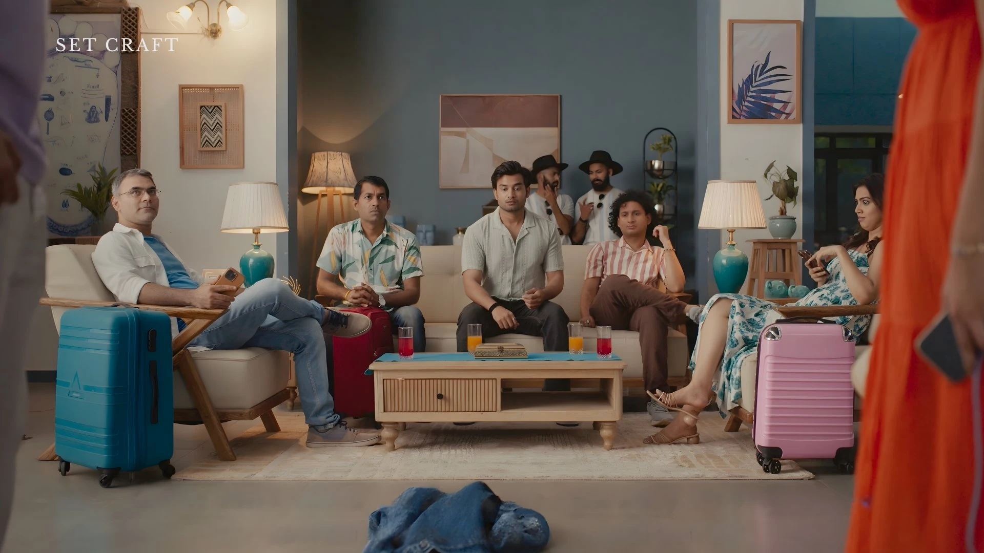 Wide shot of beach farmhouse living room set with sofa, coffee table, luggage props, and ocean-view windows.