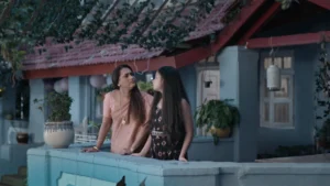 Mother and daughter standing on a blue verandah outside a traditional Goan-style house during evening light in a cinematic family commercial set design.