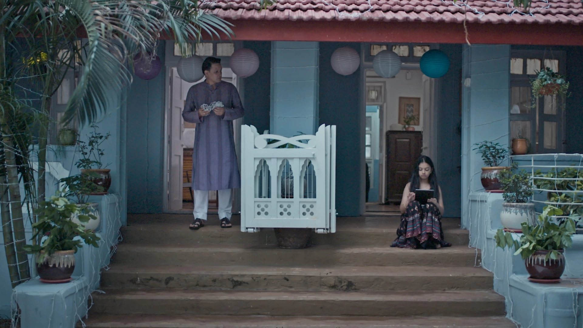 Traditional blue family house verandah with festive lanterns, tropical plants, and cinematic evening production design styling.