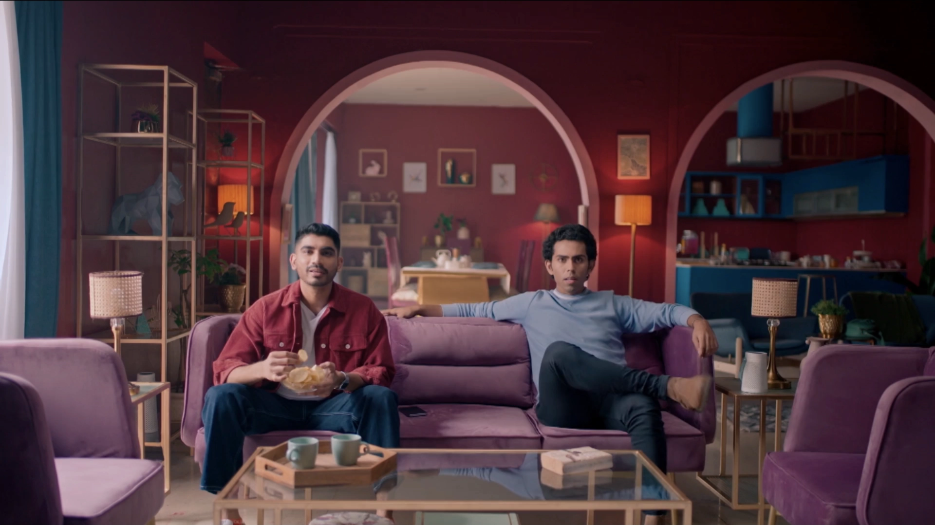 Burgundy living room set with arched architecture, purple sofas, and cinematic television commercial styling.
