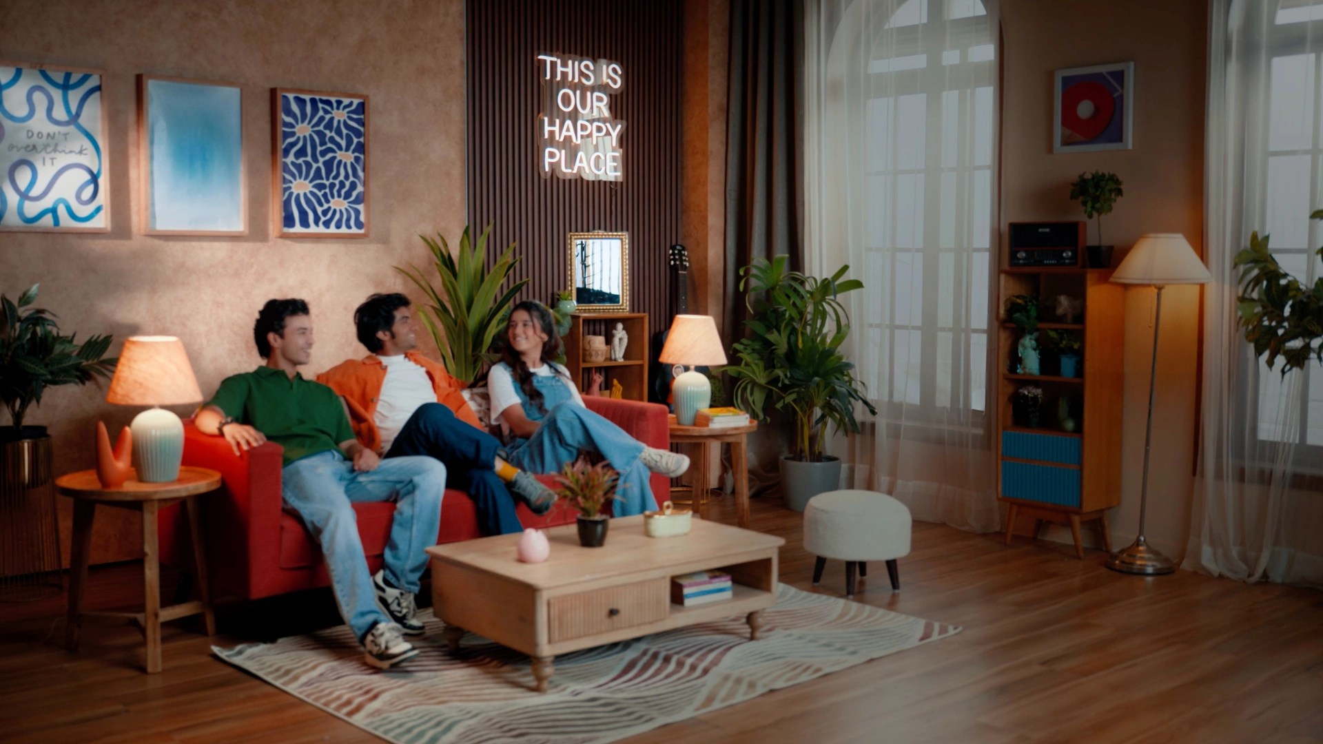 Modern living room set with neon wall sign, warm lighting, indoor plants, and contemporary commercial styling.