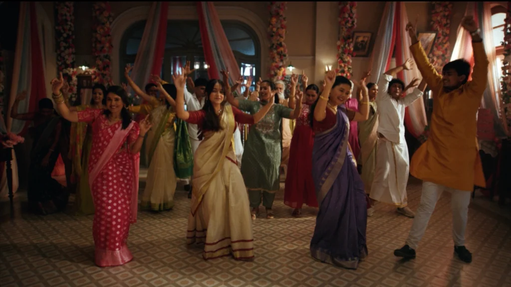 Large Indian wedding dance sequence set with floral decor, drapes, festive lighting, and traditional costumes.
