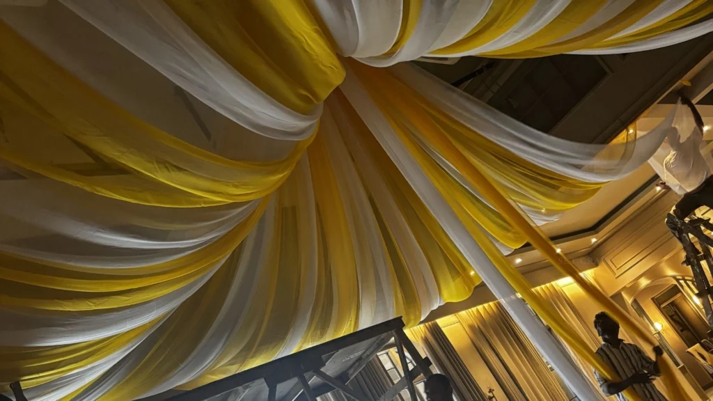 Large-scale fabric installation and lighting setup during wedding set construction.
