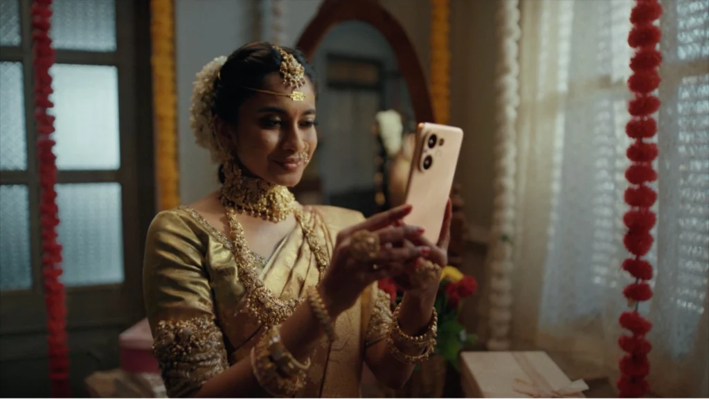 Bride in traditional South Indian attire using a Vivo smartphone inside a decorated wedding venue.