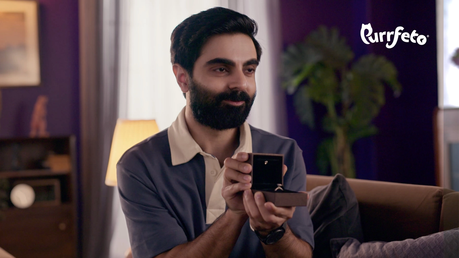 Purrfeto film still showing a man holding an open ring box against the purple living-room set